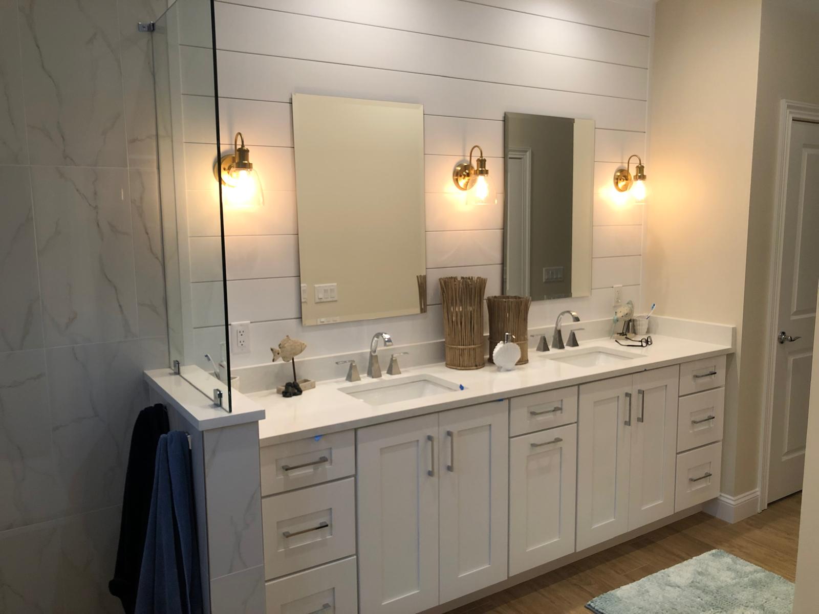 Finished bathroom remodel with double vanity, shiplap wall, mirrors, sconces, and glass shower