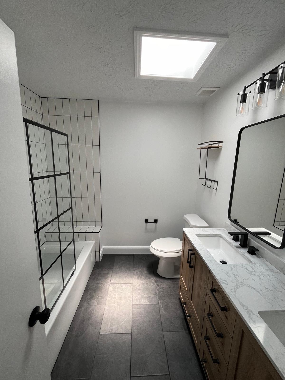 Completed bathroom remodel with tub surround, vanity, flooring, lighting, and fixtures