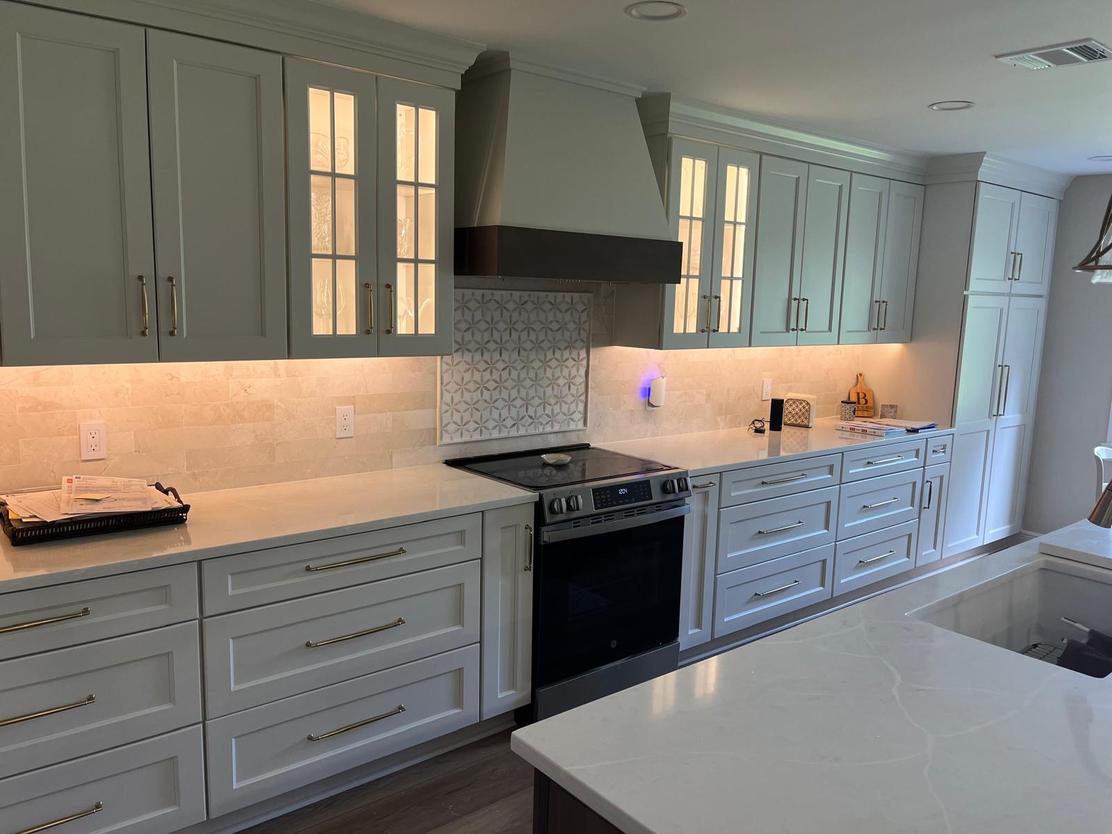 Finished kitchen remodel with gray cabinets, white counters, lighting, backsplash, and range hood